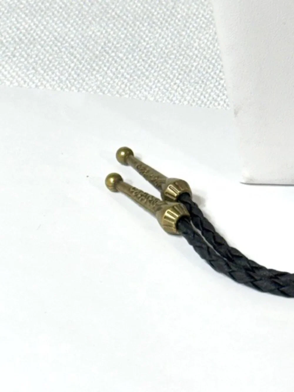 Gold-tone cowboy hat and feather, black cord western cowboy bolo tie.